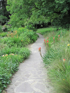 Paved path with flowers on either side and trees in the background