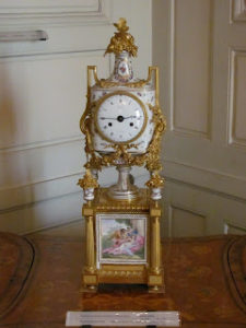 Exquisitely decorated freestanding white china clock with gold leaf (I guess?) The clock is supported on a pedestal that features a painting reminiscent of Watteau.