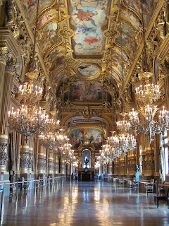 Long ornate foyer: pillars, lots of gold, paintings on the walls and ceiling, and a gleaming floor reflecting the many chandeliers