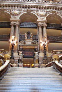 Broad staircase with balustrade on either side; at the top are two pairs of multi-story pillars and various bits of statuary, with bright lights on large pedestals.