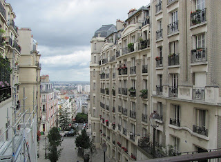 View looking down a steep hill lined with beautiful tall buildings, with a cloudy sky in the background