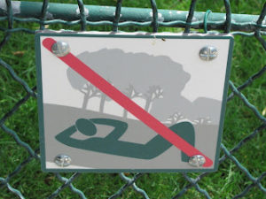Sign showing a stylized human lying on the ground, hands behind head, under trees; a red slash runs across the image on the sign