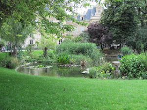 Park with immaculate lawn and beautifully landscaped pond, with a Paris neighborhood in the background