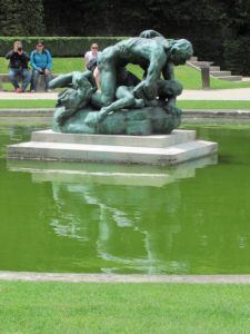 Large multi-figure sculpture in an ornamental pool. The metal sculpture is green with age.